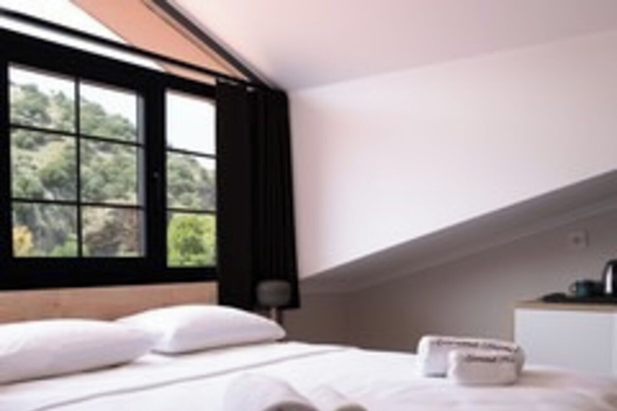 A bedroom with a bed, pillows, a window, and a bedside table.
