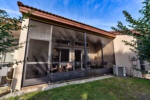 A covered outdoor patio with a table and chairs, a window, and a small air conditioning unit. - Family 2BR townhouse w/ pool access & patio (Kissimmee)