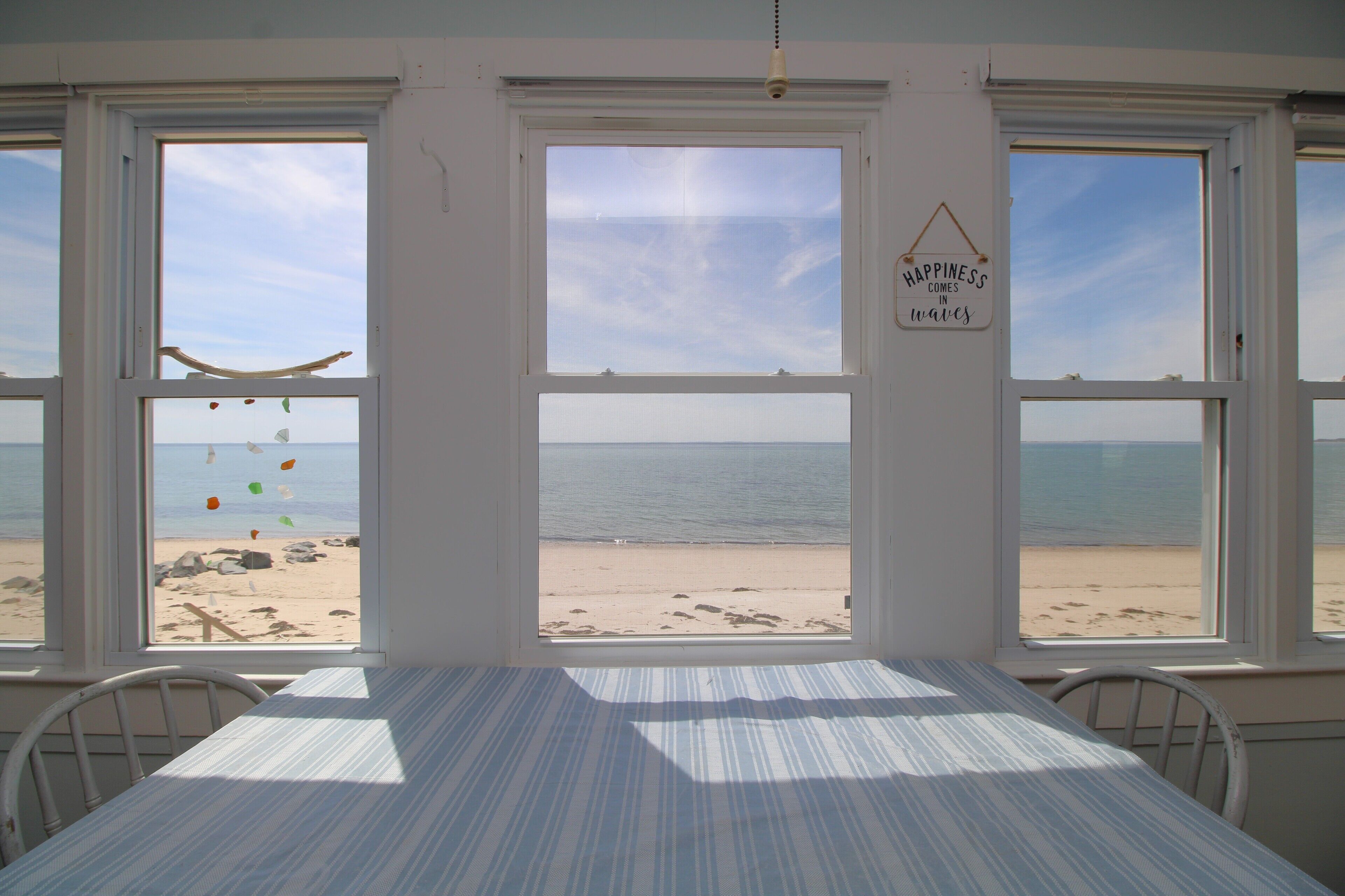Habitación con un amplio ventanal con vistas a la playa, una cama y un cartel que dice 'La felicidad llega en olas'.