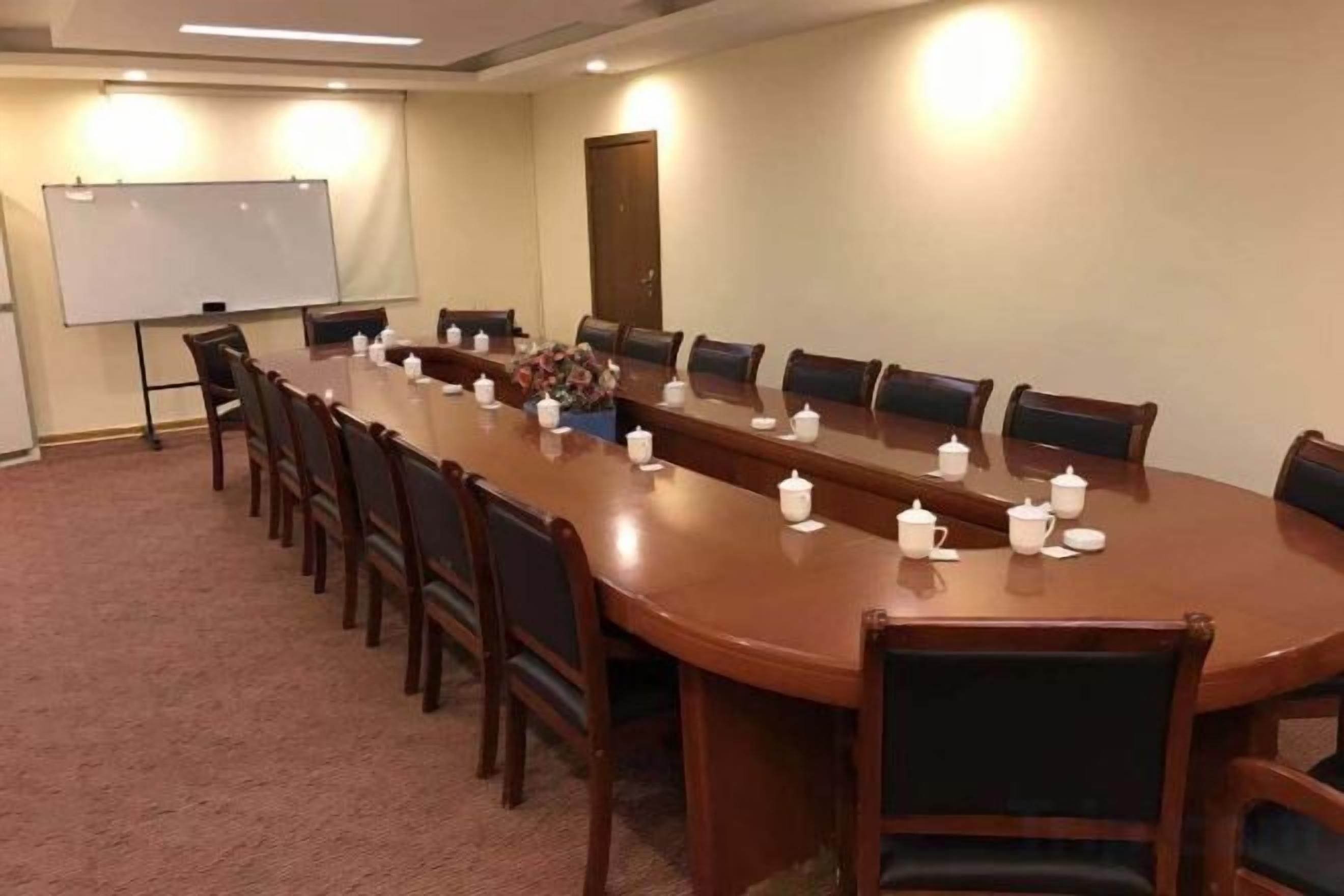 A conference room with a long table, chairs, a whiteboard, and a projector screen.