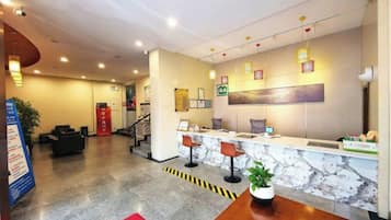 A hotel reception area with a marble counter, seating, and a staircase leading to other floors.