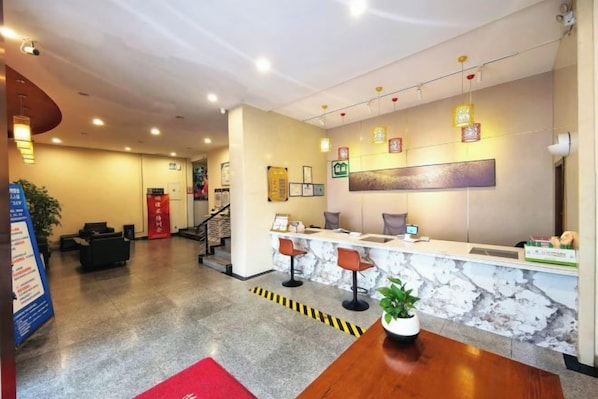 Zona de recepción de un hotel con mostrador de mármol, asientos y una escalera que conduce a otras plantas.