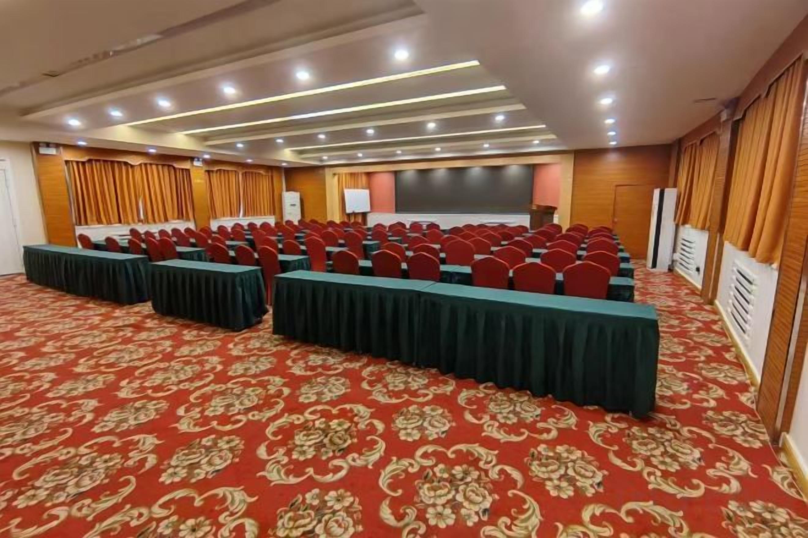 Uma sala de conferências com fileiras de cadeiras, uma mesa comprida e uma tela de projeção.