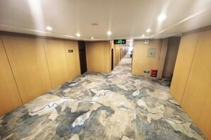 A hotel corridor with wooden walls, a patterned carpet, and a fire extinguisher on the right. - Minzu Building Express Hotel (Zhengzhou Zijing Shandong Street Subway Station) (Zhengzhou)