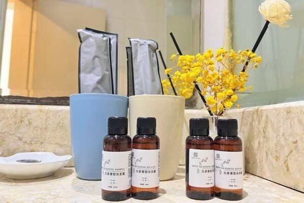 Ein Badezimmer-Waschtisch mit drei braunen Flaschen parfümierten Produkts, einer weißen Schale und einer Vase mit gelben Blumen.