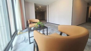 Una moderna camera d'hotel con una grande finestra, un'area salotto con due poltrone e un tavolino, e una pianta sul tavolo.