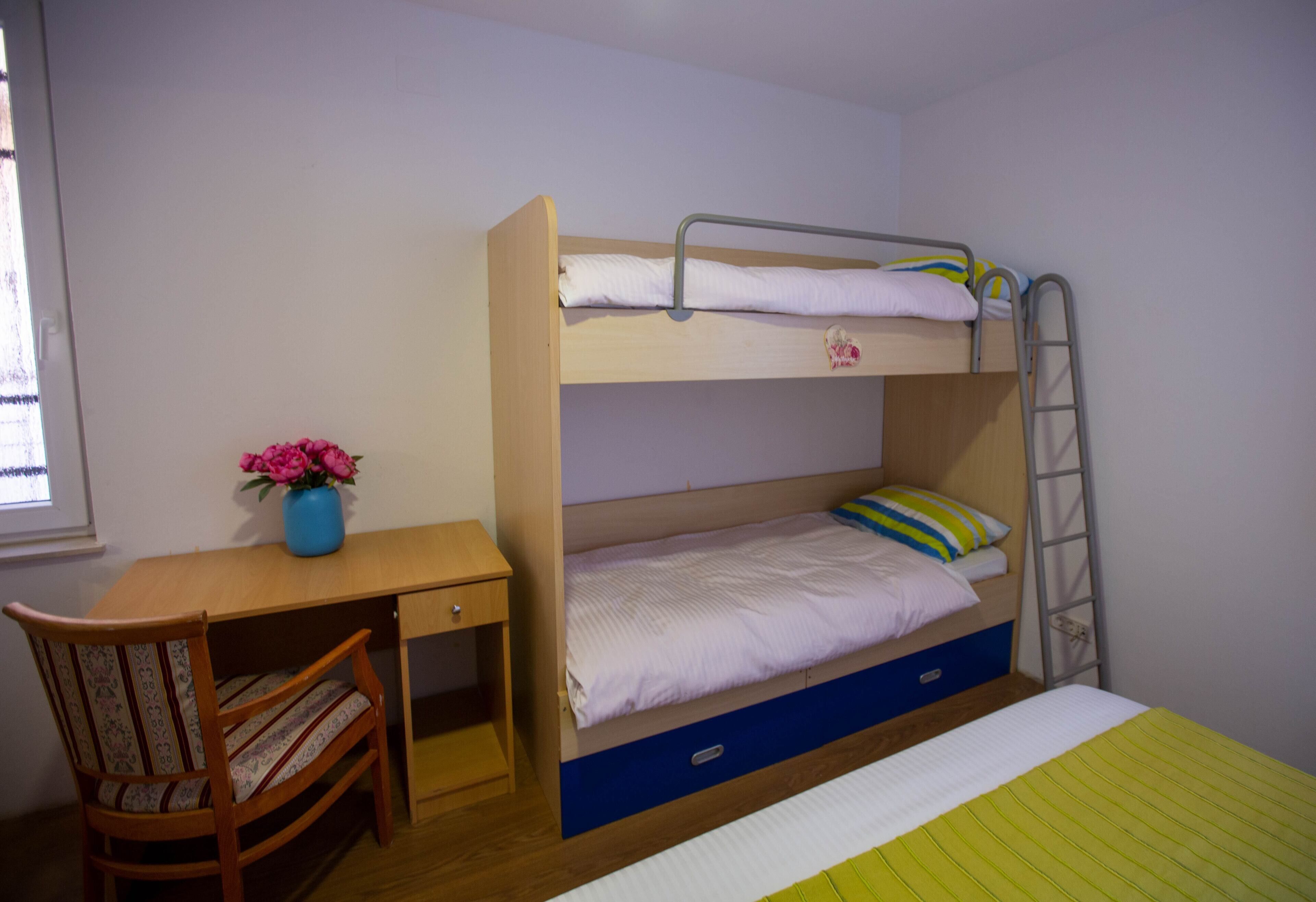 Ein Stockbett mit Schreibtisch und Stuhl, ein kleiner Tisch mit Blumen in einer Vase und eine Treppe.