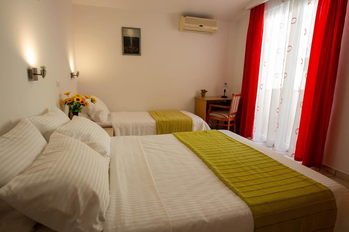 A hotel room with two beds, a desk, a chair, and a window with red curtains.