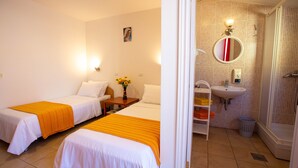 A hotel room with two single beds, a wooden nightstand with a vase of sunflowers, a bathroom with a sink, mirror, and shower. - Pansion Boris Međugorje (Citluk)