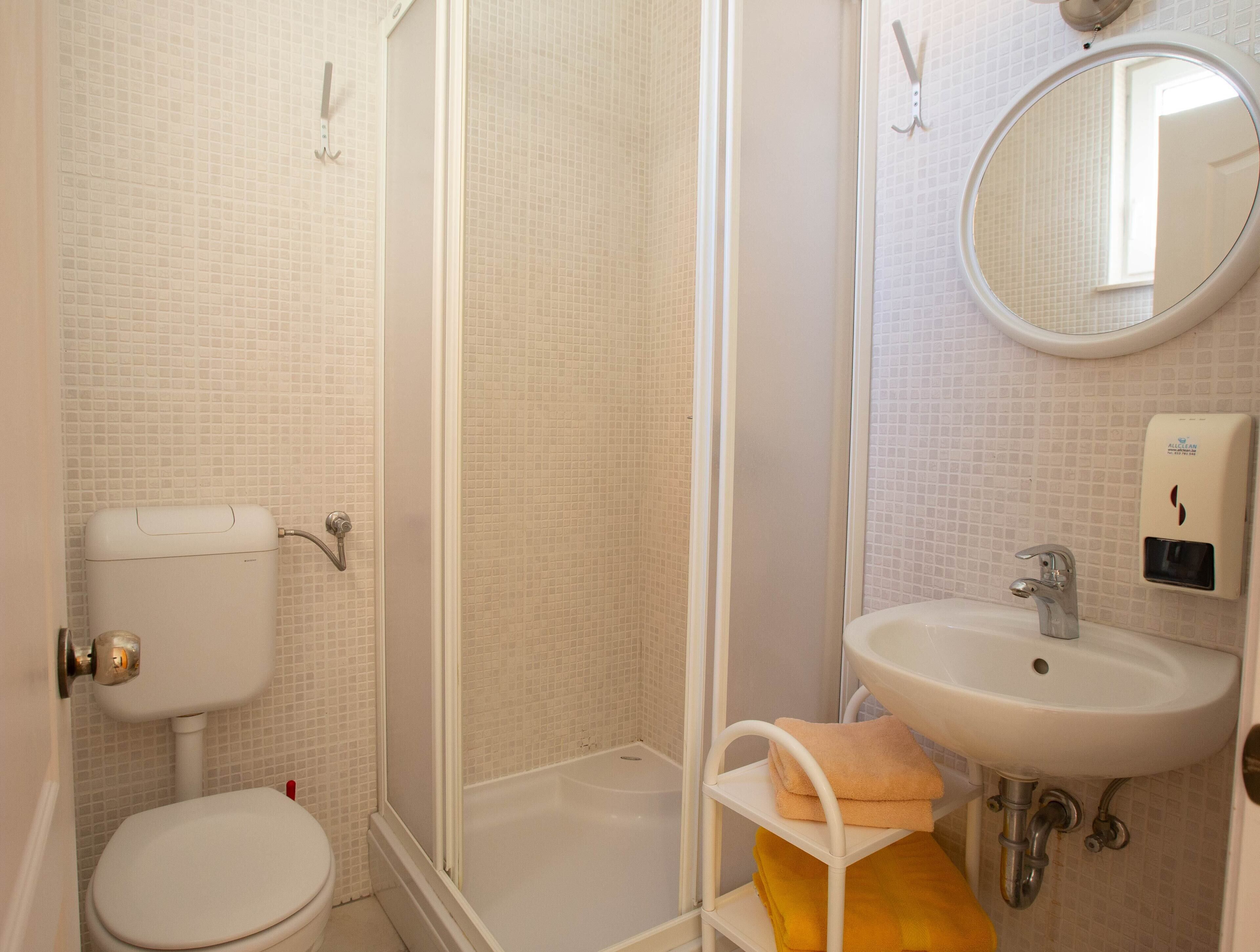 A bathroom with a toilet, shower, sink, and a mirror.