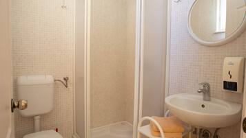A bathroom with a toilet, shower, sink, and a mirror.