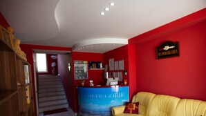 A reception area with a red wall, a blue counter, a yellow sofa, and a staircase leading to another floor. - Pansion Boris Međugorje (Citluk)