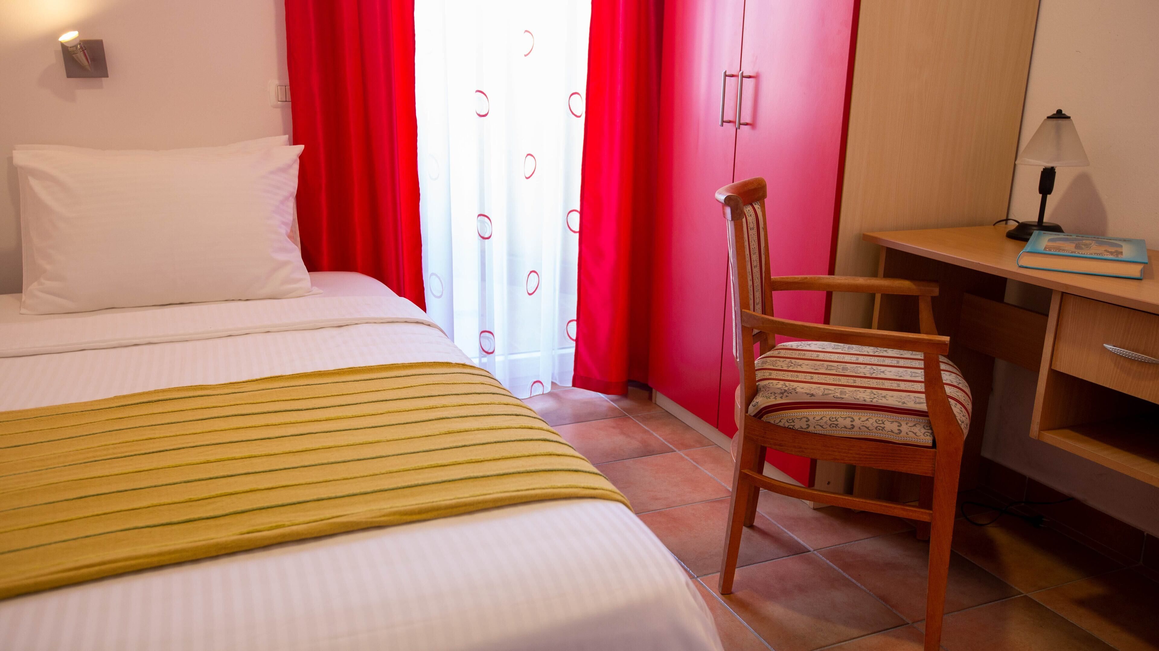 Quarto de hotel com uma cama, uma escrivaninha, uma cadeira e um abajur.