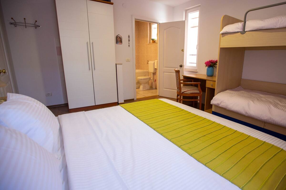 A hotel room with a bunk bed, a desk, a chair, and a bathroom visible through an open door.