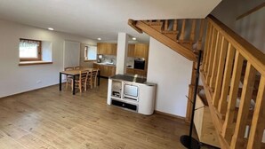 Een ruime woonkamer met een houten trap, een eettafel en een kitchenette.