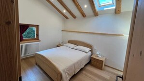 Een slaapkamer met een bed, nachtkastje en een raam met uitzicht op bomen.