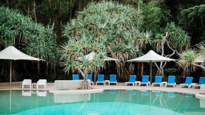 A pool area with blue lounge chairs and white umbrellas, surrounded by tropical plants.