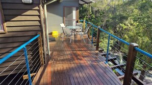 A wooden deck with a blue railing, a table with chairs, and a view of a forested area.