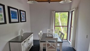 A dining area with a table and chairs, framed pictures on the wall, and a window with a view of trees.