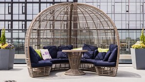 Un área de estar al aire libre con muebles de mimbre, una mesa, cojines y plantas en macetas.