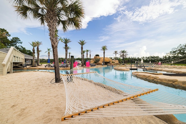 A pool area with a hammock, palm trees, and a building in the background.