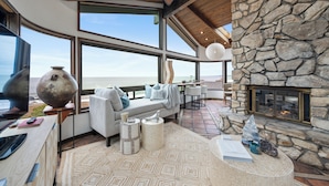 A modern living room with a stone fireplace, large windows, and a view of the ocean.
