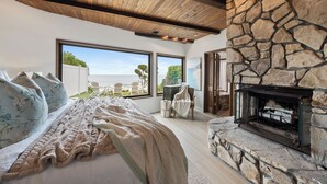 A bedroom with a large bed, a stone fireplace, and a view of the outdoors.