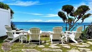 A patio with four Adirondack chairs facing a beach with the ocean.