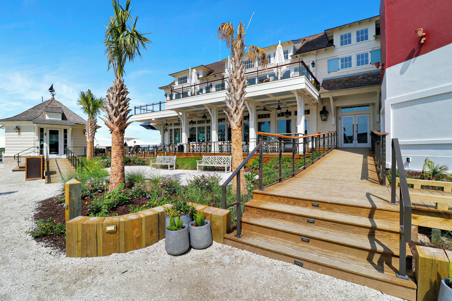 Een strandhotel met een houten terras, buiten zitplaatsen en een groot gebouw met meerdere balkons.