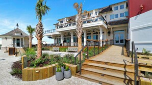 A beachfront hotel with a wooden deck, outdoor seating, and a large building with multiple balconies.
