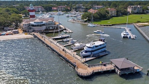 A marina with multiple boats docked, a pier extending into the water, and buildings in the background.