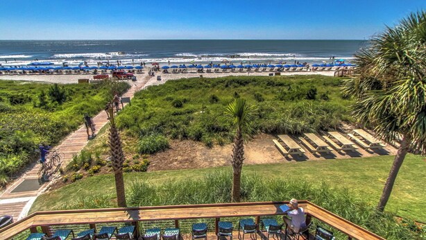 A beach view with a wooden deck, lounge chairs, and a pathway leading to the beach.