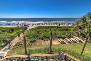 Blick auf einen Strand mit einer Holzterrasse, Liegestühlen und einem Weg zum Strand.