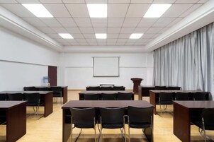 Un salón de conferencias con una pizarra, una pantalla de proyector y un amplio ventanal con cortinas.
