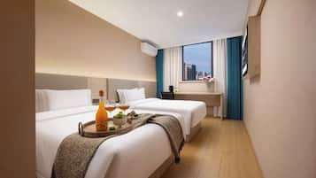 Quarto de hotel com duas camas, uma pequena mesa de escritório, uma janela com cortinas e uma bandeja com bebidas e frutas sobre a cama.