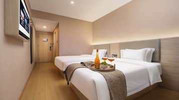 Quarto de hotel com duas camas, piso de madeira, televisão fixada na parede e um recipiente com garrafa e copos sobre a cama.
