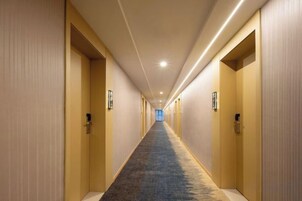 Un couloir d’hôtel avec des revêtements de sol en moquette, des portes de chaque côté et un éclairage au plafond.