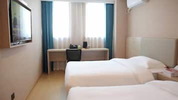 Habitación de hotel con dos camas, un escritorio con silla, televisor montado en la pared y una ventana con cortinas.