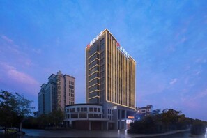 Un hotel moderno con un diseño vertical llamativo, varios pisos y una entrada bien iluminada.