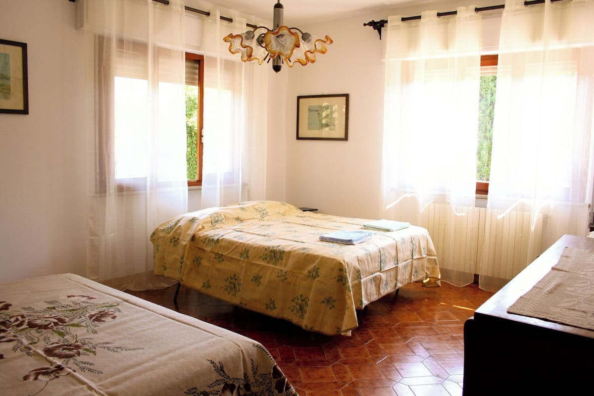 A bedroom with a bed, a bedside table, a chair, and a window with curtains.