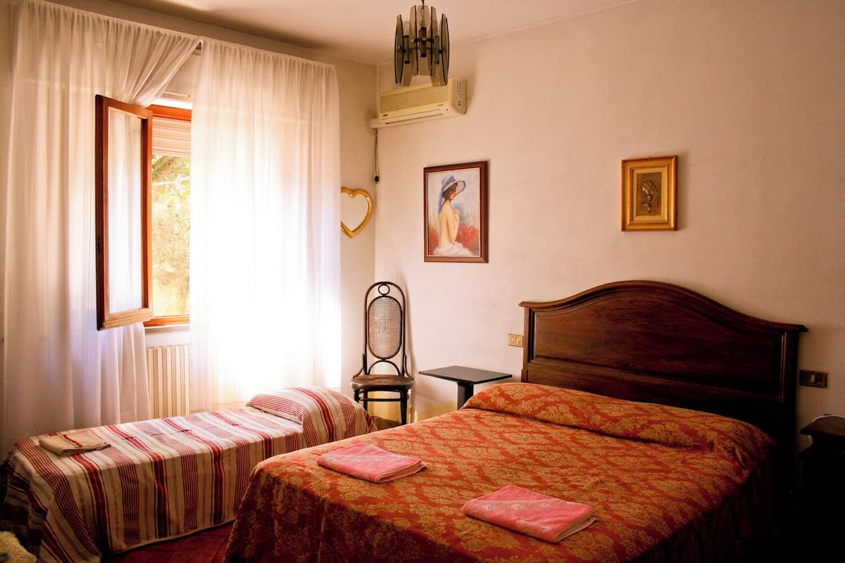 A hotel room with two single beds, a wooden headboard, a small table, a chair, and a window with curtains.