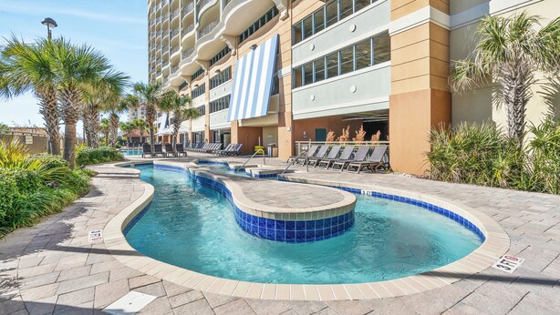 A hotel with a swimming pool, lounge chairs, and palm trees.