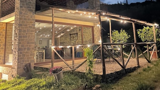 A modern house with a stone facade, large windows, and a covered outdoor area with string lights. - TUSCANY DETACHED HOUSE INCREDIBLE PANORAMA, LARGE GARDEN 5 MIN FROM AREZZO (Toscana)