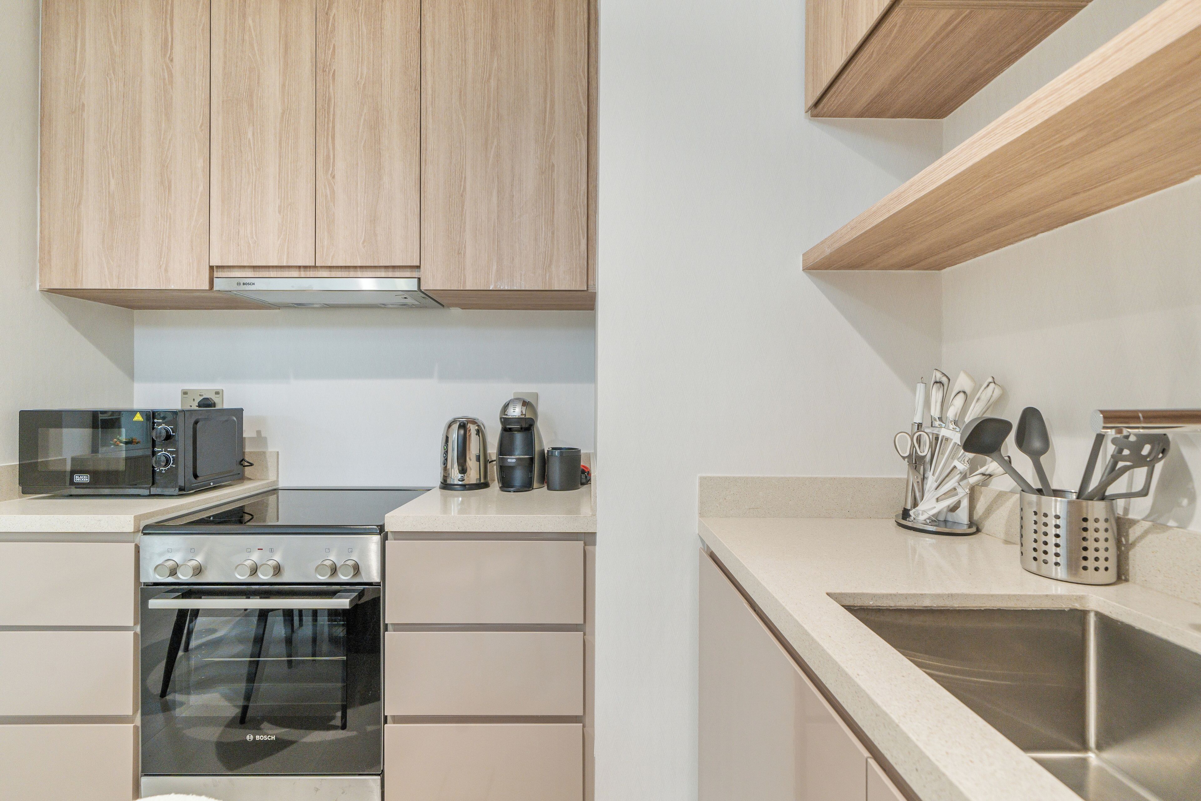 A modern kitchen with wooden cabinets, a Bosch oven, a microwave, a coffee maker, and a stainless steel sink.