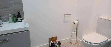 A bathroom with a white sink, toiletries, a toilet, and a basket of personal care items.
