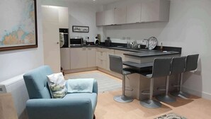 A modern kitchen with a dining area, featuring a sofa, bar stools, and a kitchen island. - Seaview Loft 20 Portrush (Portrush)