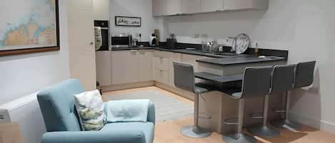 A modern kitchen with a dining area, featuring a sofa, bar stools, and a kitchen island.