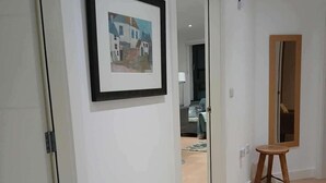 A hallway with a framed picture on the wall, a wooden stool, and a door leading to another room. - Seaview Loft 20 Portrush (Portrush)