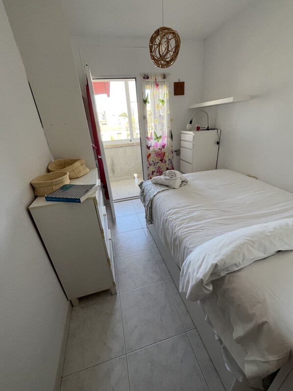 A bedroom with a bed, a desk, a chair, a hanging light fixture, and a window with curtains.
