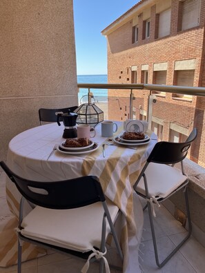 A balcony with a table set for two, featuring a tablecloth, plates of food, cups, and a coffee maker.